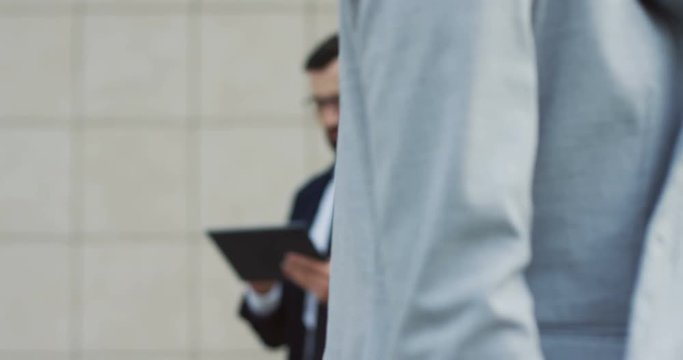 Close up of the woman in a jacket going in and out of the camera while using smartphone. Man in a suit and tue with tablet computer in hands on the blurred background.