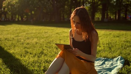 Relaxed young woman using tablet computer outdoors. Steadicam smooth shot of typing and Internet surfing using digital pad. Middle shot. - Powered by Adobe