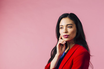 Young woman thinking with hand on face looking off camera, isolated on pink studio background