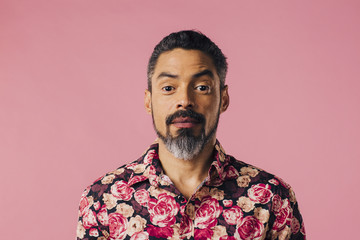 Portrait of a friendly, mature man with silver beard and flowery shirt, isolated on pink studio background - obrazy, fototapety, plakaty