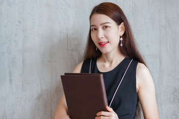 Beautiful young business woman and holding books on gray wall background.