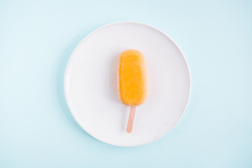 One raw vegan mango popsicle from above. Pastel blue background. Minimalism food photography. Geometric style. Copyspace