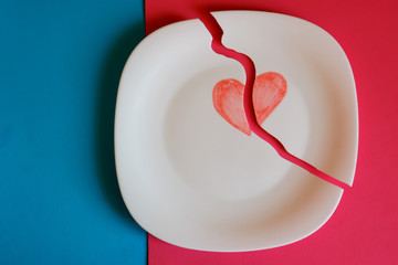 Crack. Broken plate with a painted heart on a red and blue background.