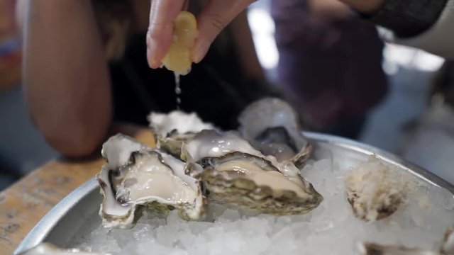 SLOWMO Closeup, hand squeezes lemon over oysters on ice