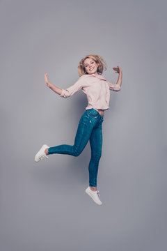 Full body length size portrait of attractive beautiful curly-haired blonde caucasian young girl wearing casual shirt and jeans flying in air. Isolated over grey background