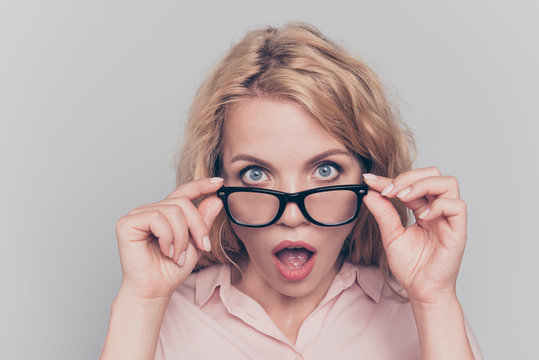 Wow! Surprised pretty young blonde touching looks over the glasses wide open eyes and mouth with surprise isolated on gray background