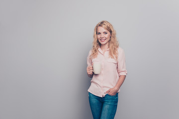 Charming girl in pink shirt holds in her hand white mug with drink and looks directly into the camera smiling isolated on gray background with copy space for text