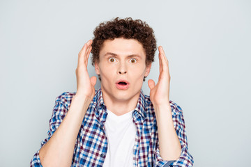 Young attractive shocked guy raising hands to head, copy blank empty space. Isolated over grey background