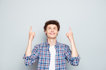 Cute brunet man in casual outfit gesturing up with fingers isolated on light gray background with...