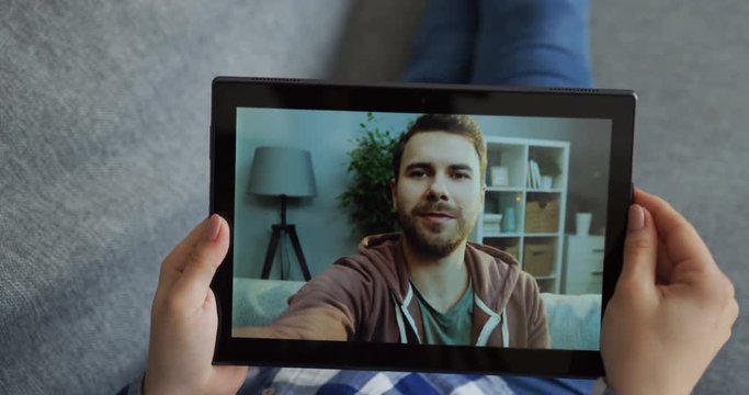 Close up of the black tablet device in hands of the caucasian woman who videochatting on the web cam with a man, her friend or boyfriend. Top view.