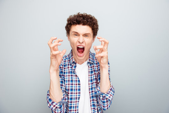 Portrait of an angry, aggressive young man who screams look at the camera isolated on light gray background