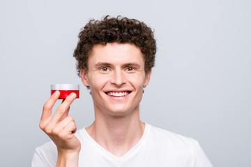 Portrait of model guy having red jar with effective cream for face and under eyes looking at camera isolated on light gray background