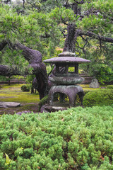 Fototapeta na wymiar View of an old stone lantern in gardens of the Nijo castle during a rainy summer day