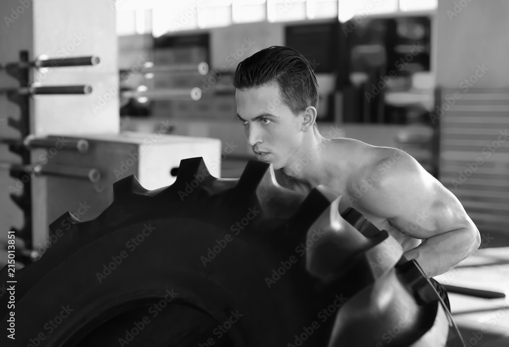 Wall mural young muscular man training with heavy tire in gym, black and white effect