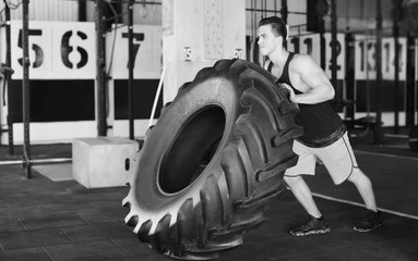 Obraz na płótnie Canvas Young muscular man training with heavy tire in gym, black and white effect