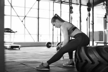 Fototapeta na wymiar Young muscular woman sitting on heavy tire in gym, black and white effect