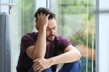 Lonely depressed man near window at home