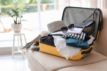 Open yellow suitcase with different clothes packed for journey at home