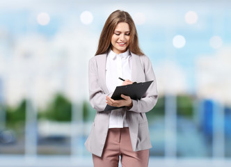 Young businesswoman in elegant suit with clipboard on blurred background