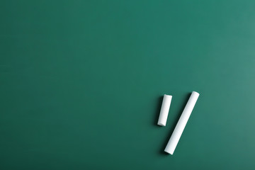 Pieces of chalk on green background, top view