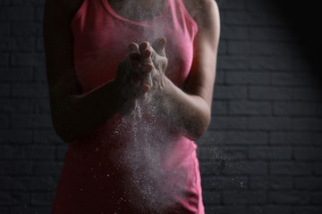 Young woman applying chalk powder on hands against brick wall