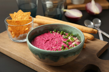 Bowl with tasty beet hummus, bread sticks and chips on table
