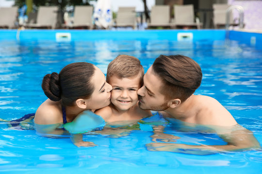 Young family with little son in swimming pool on sunny day