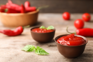Bowls with spicy chili sauce on wooden table