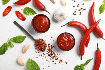 Flat lay composition with bowls of hot chili sauce and different spices on light background