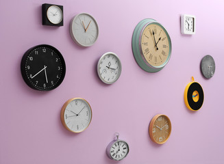 Many different clocks hanging on color wall. Time of day
