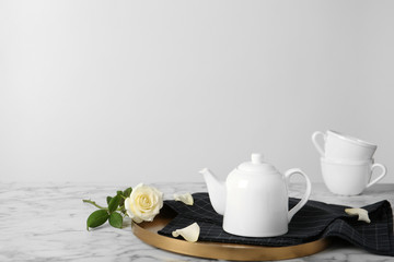 Tray with teapot and rose on table against light background