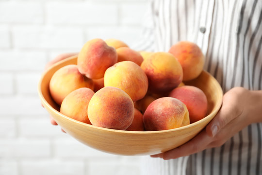 Woman holding bowl with delicious ripe peaches, closeup