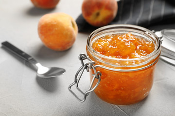 Jar with tasty peach jam on table