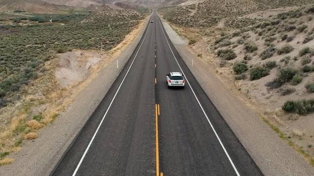 drone shot of a car driving off into the distance of a very long and straight scenic road.