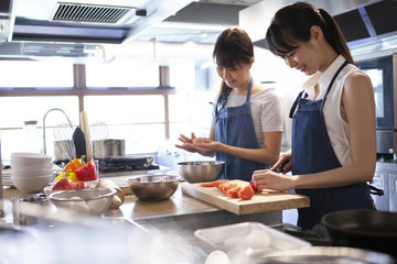 料理教室でハンバーグを整形し、トマトを切っている参加者の女性