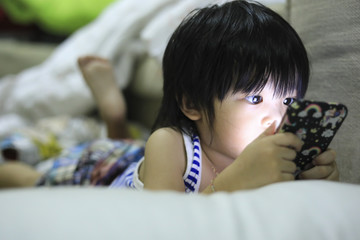 Obraz premium Cute Asia kid playing games on smartphone