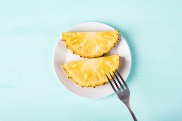 Slice pineapple on white plate with fork for eating, top view, tropical fruit