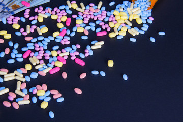 Variety of colorful pink and blue spilled pills on a black background with text space. Healthcare expenses, savings, insurance concept. Healthy lifestyle to improve health