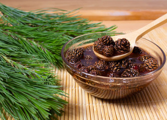 Still-life, jam from cones, in a glass bowl and a wooden spoon. Around the spruce branches.