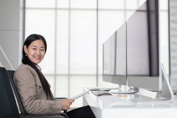 Beautiful young Asian Sitting in  modern office happily, there are many computer monitors, ideas for joyful working.