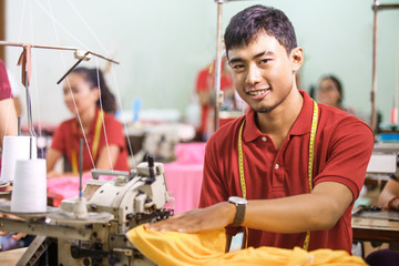 man smiling while sewing on a sewing machine at a clothing facto