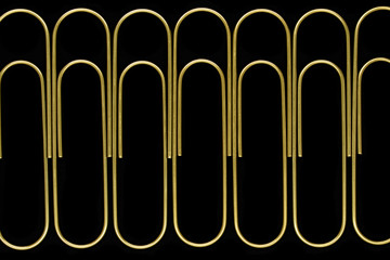 Group of sharp and clear view of golden paperclips standing in line on black background surface