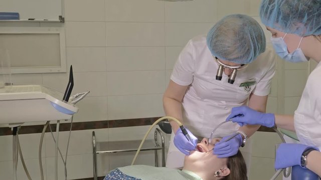 Woman at dentist clinic gets dental treatment to fill a cavity in a tooth. Dental restoration and composite material polymerization with UV light and laser. The doctor works with an assistant.