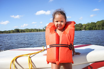 Preschool age girl wearing a life jacket and standing in a boat on a lake