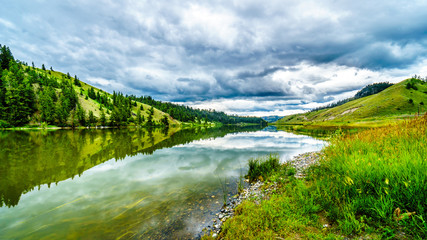 Fototapeta na wymiar Dark Clouds and surrounding Mountains reflecting on the smooth water surface of Trapp Lake, located along Highway 5A between Kamloops and Merritt in British Columbia, Canada
