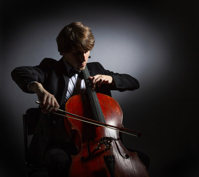 Young man playing the cello. Portrait of the cellist on a dark background.