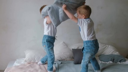 Twin boys toddlers are lying on the bed, throwing pillows, jumping and laughing.