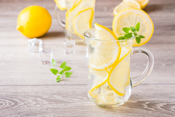 Refreshing cold mineral water with lemon, mint and ice cubes in glasses on a wooden table