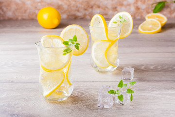 Melting ice cubes, fresh mint leaves and water with lemon in a glass on a wooden table