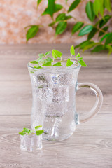 Cold mineral water with ice cubes and mint leaves in a transparent glass on a wooden table